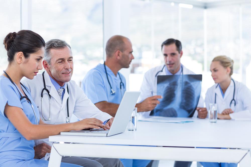 Doctors sitting at a table using computers and looking at an x-ray